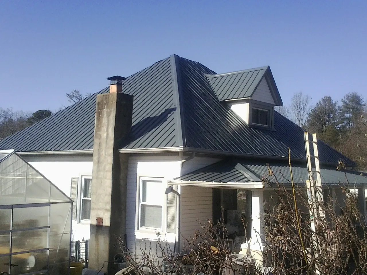Dark blue standing seam metal roof on a white farmhouse with dormer — Slate & Tile Roof Repair by Roofing Brothers in South Sterling