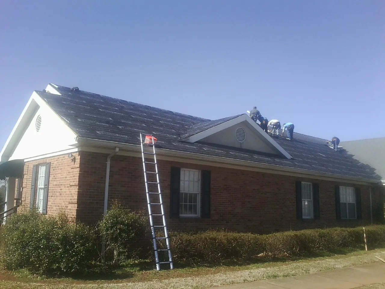Crew tearing shingles off a brick ranch roof with a ladder set — Emergency Roof Repair work by our crew in South Sterling
