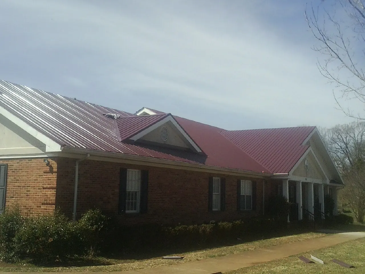 Red metal roof with gabled entries on a long brick building, from a Hail Damage Roof Repair job in South Sterling
