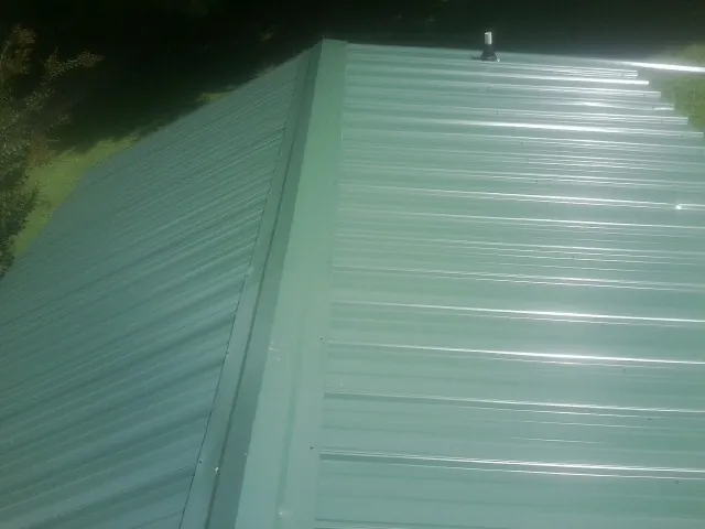 New green metal panels meeting at the ridge of a roof — Flat Roof Repair work by our crew in South Sterling