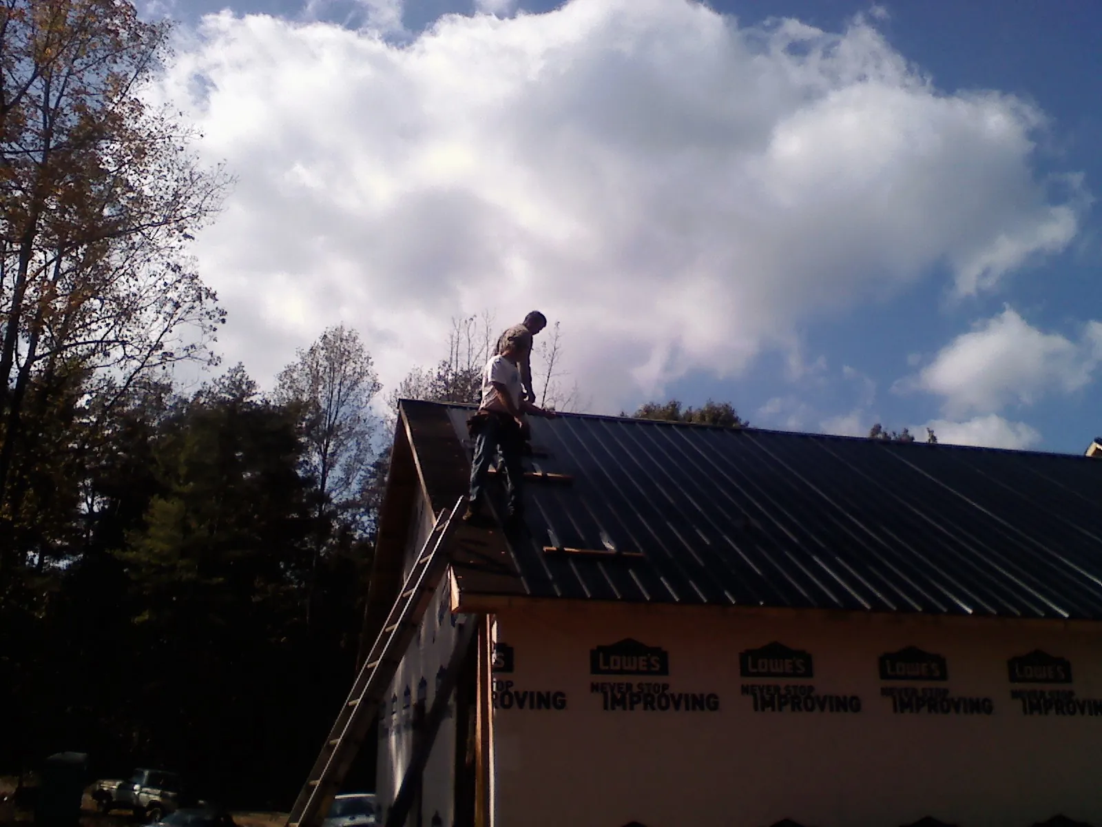Roofer fastening dark metal panels high against a cloudy sky, from a Roof Inspection job in South Sterling