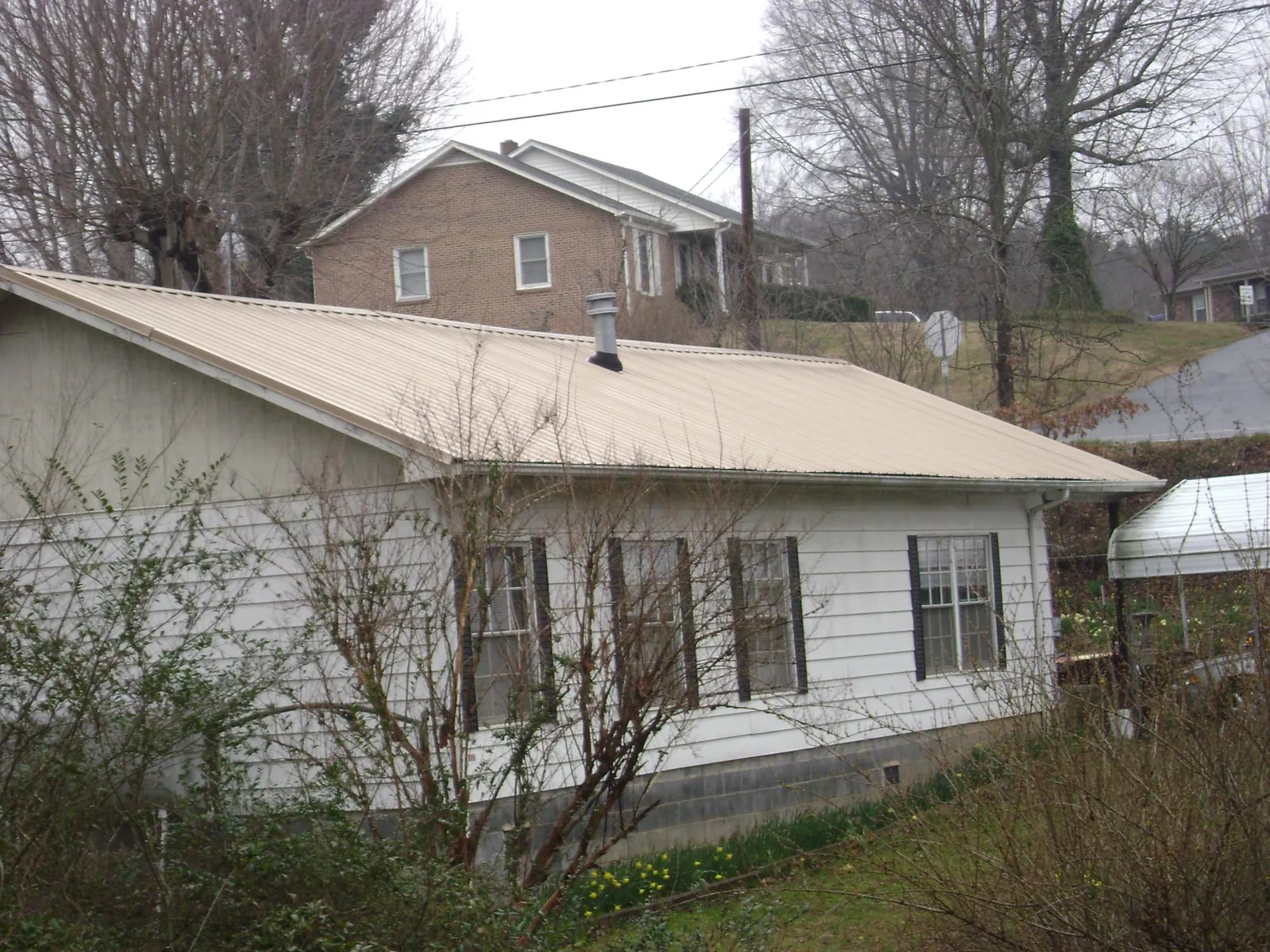 Tan metal roof on a white sided house set into a hillside in South Sterling